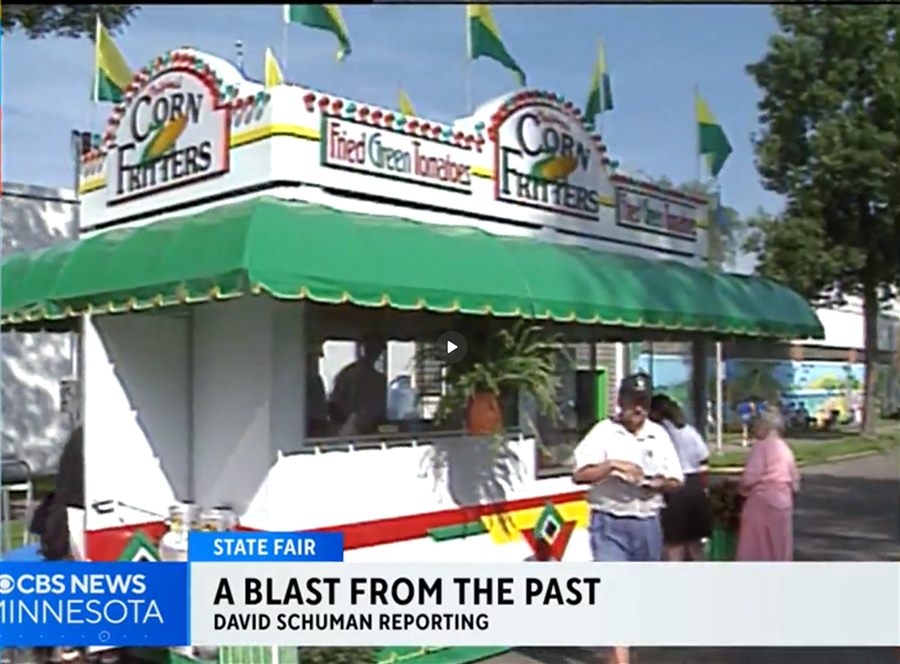 The original Corn Fritters and Fried Green Tomatoes booth in 1993: a white stand with a green striped awning, rooftop signs, and yellow and green pennant flags