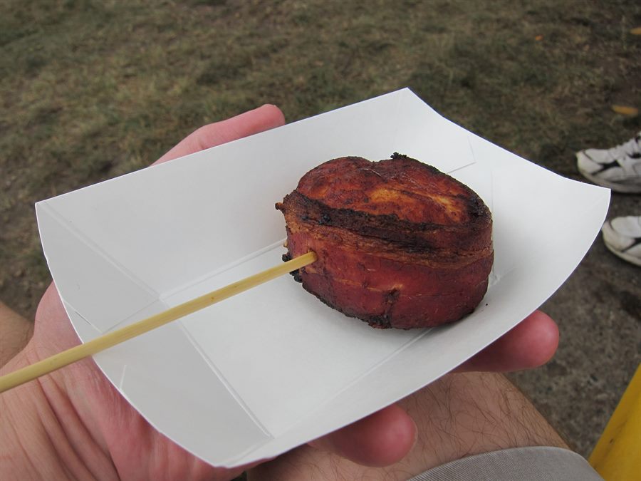 A bacon-wrapped turkey tenderloin on a wooden skewer in a white paper tray