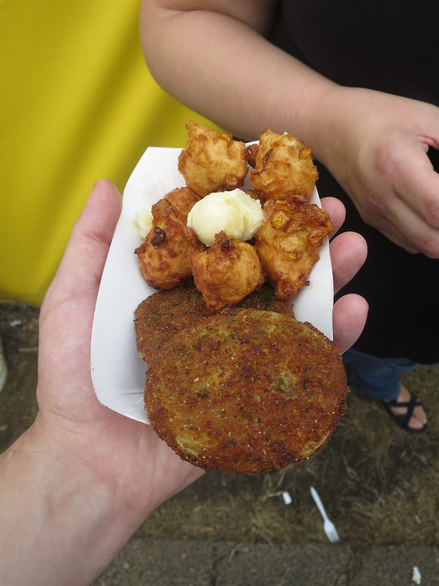 Corn fritters arranged around a scoop of butter with a large fried green tomato, small hands reaching in