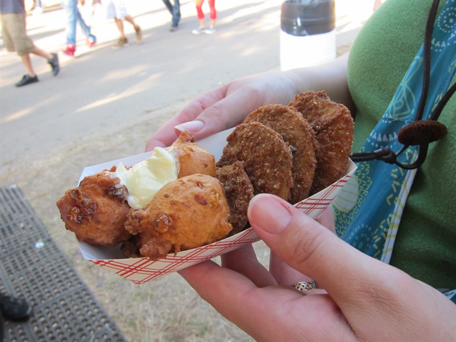 Red plaid paper boat of corn fritters topped with honey butter, fried green tomatoes behind
