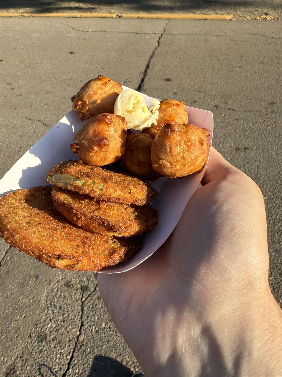 A tray of fried green tomatoes and corn fritters held over cracked asphalt in morning light