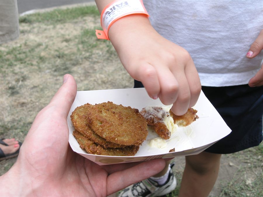 A paper tray of fried green tomatoes as a child's hand reaches in to grab a piece